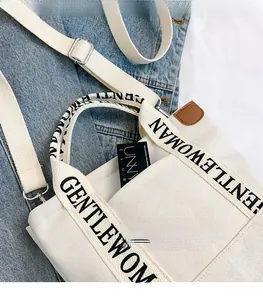 Detail of canvas tote bag with Gentlewoman logo handle and brown leather accent on denim