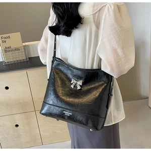 Close-up of black pleated underarm bag with silver bow detail and logo on PU leather