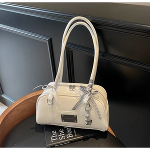 Detail of white glossy patent leather bag with bows, heart pendant, and metal nameplate
