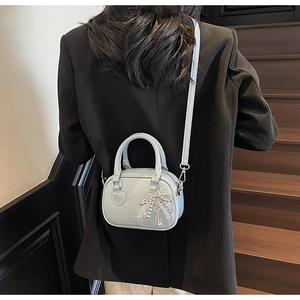 Detail of light blue Boston bag with heart embossing and pearl bow charm on black suit