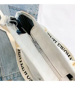 Detailed shot of metal zipper pull on cream canvas tote with striped lining and strap