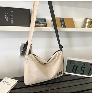 Detail of beige nylon crossbody bag featuring zipper closure and adjustable black shoulder strap
