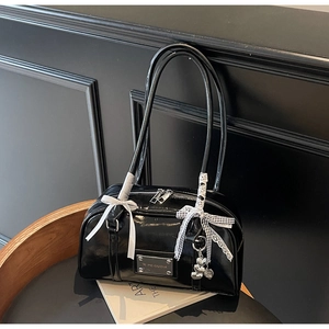 Detail of glossy black patent leather shoulder bag with bows and heart charm on dark wood