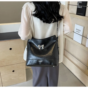 Detail of a black bucket shoulder bag featuring a silver metal bow and adjustable strap