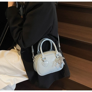 Detail of light blue mini Boston bag with heart stitching and silver bow charm accessory