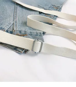 Detail of white woven canvas belt with silver metal slide buckle on denim fabric