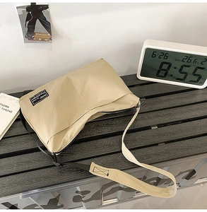 Detail of beige nylon crossbody bag showing water-resistant fabric and brand logo tag