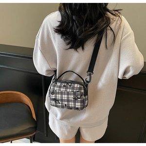 Detailed view of checkered floral canvas crossbody bag featuring dual zippers and woven label