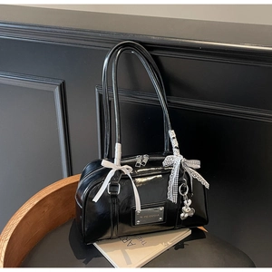 Close-up of black glossy PU leather bag with white ribbon bow and silver heart bear charm