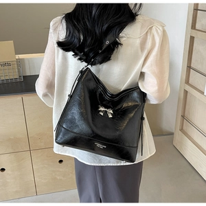Close-up of black glossy leather tote bag featuring a silver bow and logo detail
