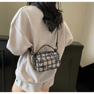 Detail of floral patterned small square crossbody bag with black woven handle and strap