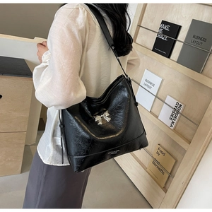 Detail of black glossy wrinkled leather tote bag with silver metal bow and shoulder strap