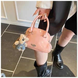 Detalle de un bolso de concha en charol rosa brillante con un llavero de oso de peluche