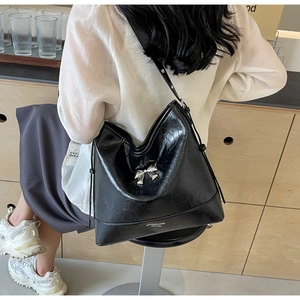Detailed macro of a black glossy pleated leather Hobo bag with a silver metal bow buckle