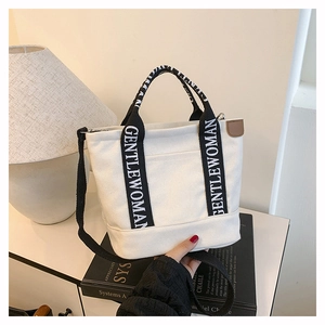 Detail of white canvas tote bag on books featuring logo handles and side leather tag