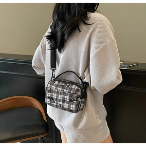 Detail of checkered crossbody bag featuring cartoon cat motif and wide strap