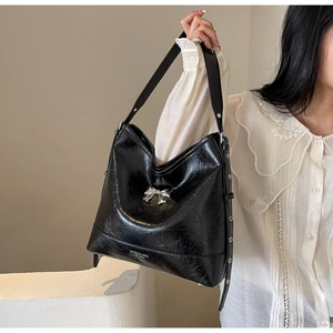Detail of black wrinkled leather tote bag featuring a silver bow buckle and wide strap