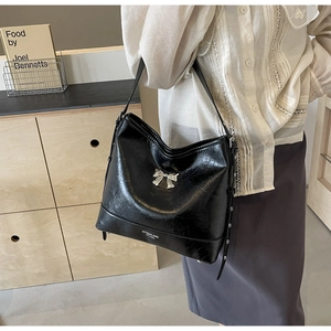 Detail of black glossy PU tote with silver metal bow and shoulder strap in lifestyle setting