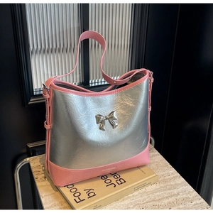 Detail of silver crinkled shoulder bag with pink leather trim and metal bow on marble
