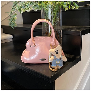 Detalle del bolso de charol rosa con forma de concha y colgante de oso en escaleras negras