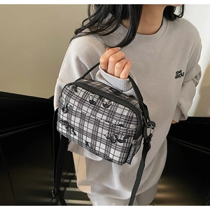 Detail view of the black and white checkered canvas bag with brand woven label and strap