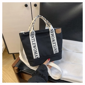 Close-up of black canvas tote bag with GENTLEWOMAN logo straps and leather detail