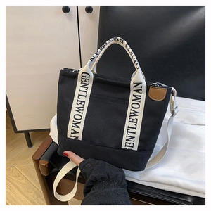 Detail of black canvas tote bag showing white GENTLEWOMAN logo strap and leather patch