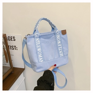 Detail of light blue canvas tote bag featuring branded white straps and brown leather trim