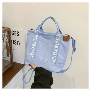 Close-up of light blue canvas tote bag with white GENTLEWOMAN branded handles and leather trim