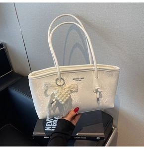 Détail d'un cabas blanc texture serpent avec breloque cœur perle et lettrage de marque