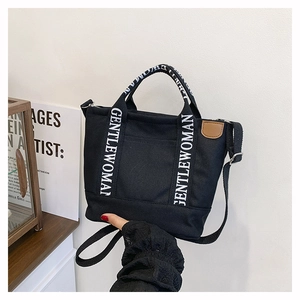 Detail of black canvas tote bag showing GENTLEWOMAN handles and adjustable shoulder strap