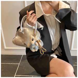 Bolso de mano plateado con forma de concha y amuleto de osito, llevado por modelo