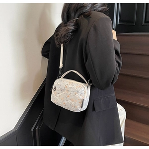 Detail of white floral lace crossbody bag shown with adjustable shoulder strap and handle