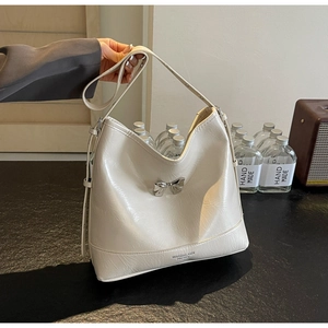 Detail of a creamy white glossy leather shoulder bag with a silver metal bow accent