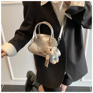 Detalle de un bolso plateado metalizado con forma de concha y un colgante de osito