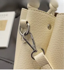 Detail of silver metal hook and pebble grain texture on off-white leather bucket bag