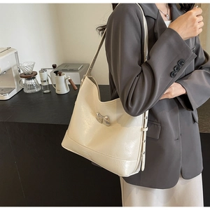 Close-up of cream underarm bag featuring silver bow metal buckle and pleated texture