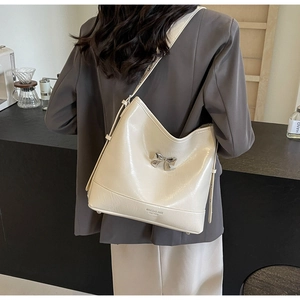 Close-up of cream leather shoulder bag with a silver metal bow accent and logo detail