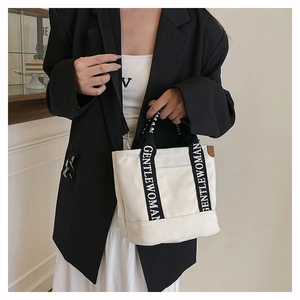 Detail of canvas tote bag showing branded handles and adjustable crossbody shoulder strap