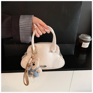 Detalle de bolso crema con cremallera plateada y colgante de osito de peluche suave