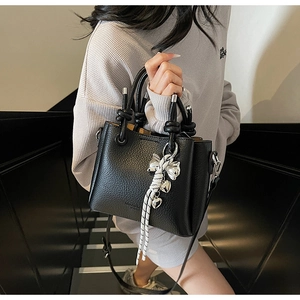Detail of black lychee leather bucket bag with white woven knot and metal charms