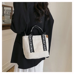 Detail view of the black logo strap and leather tag on a stylish canvas tote bag