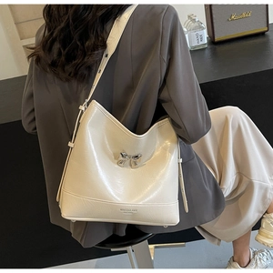 Detail of a creamy white hobo bag featuring a silver bow buckle and adjustable strap