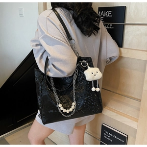 Detail of black snake-embossed tote bag with silver chain and white cloud plush charm