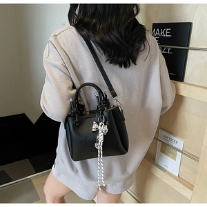 Detail of black lychee grain leather bucket bag with silver bow tassel and long strap