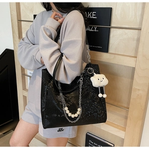 Detail of black snakeskin tote bag with pearl chain and plush cloud charm accessory