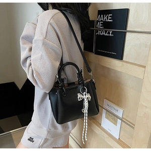 Detailed view of black litchi pattern leather bucket bag with white woven knot charm