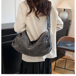Detail of a large dark denim hobo bag featuring contrast stitching and adjustable wide strap
