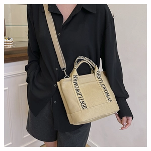 Detail of beige canvas tote with black logo strap and adjustable shoulder crossbody strap