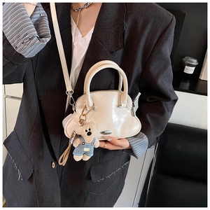 Detalle de bolso de concha blanco brillante con asa metálica y colgante de osito